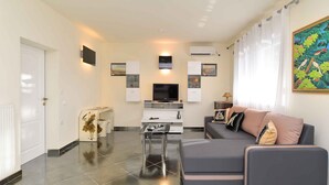 Una sala de estar moderna con un sofá gris, una mesita, un televisor y un mueble blanco.