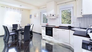 Una cocina moderna con armarios blancos, encimera negra y zona de comedor con sillas negras.