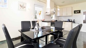 Una cocina moderna con armarios blancos, una mesa de comedor negra y sillas. Hay cuadros en la pared y una lámpara colgante sobre la mesa.