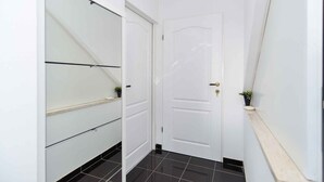 Un pasillo estrecho con una puerta blanca, un ventanal corredero y una pequeña planta en la pared.