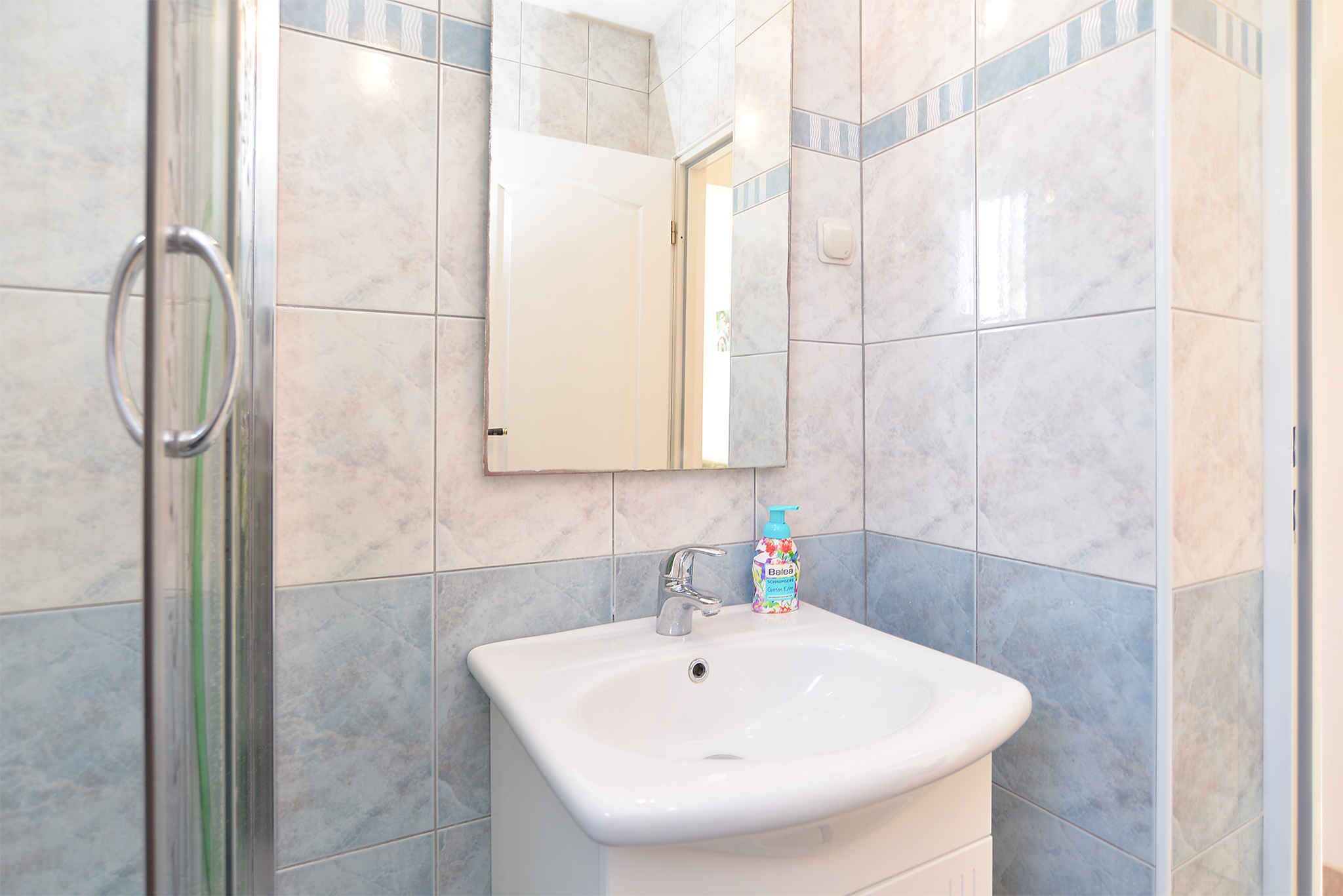 Een badkamer met een witte wastafel, een spiegel en een douchedeur.