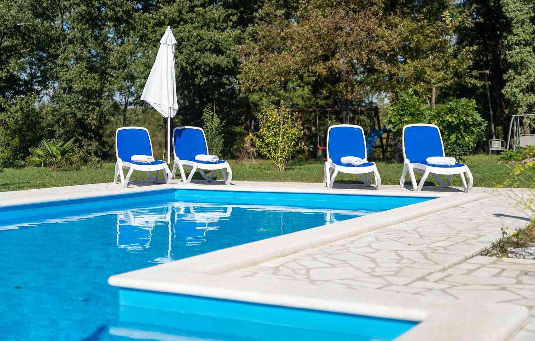 A swimming pool with four blue and white lounge chairs and a white umbrella.