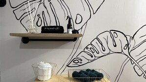 A bathroom with a white toilet, a trash bin, and two shelves with toiletries and a decorative wall art.