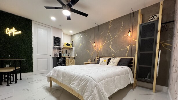A modern bedroom with a bed, a desk, and a kitchenette.