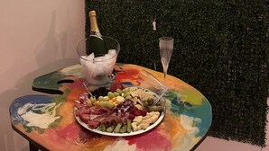 A table with a colorful tablecloth, a plate of assorted cheeses, a bottle of champagne, and two glasses.