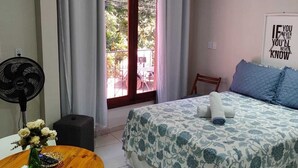 Un dormitorio con cama, escritorio, silla, ventilador y ventana con cortinas.