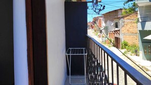 Un balcón estrecho con un tendedero de metal, techo de madera y vistas a un coche rojo y edificios al fondo.