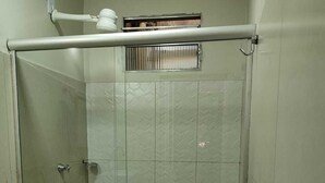 Un pequeño box de ducha cerrado con puerta de cristal, un inodoro y un lavabo con dispensador de jabón.