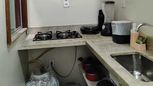 Cocina compacta con estufa a gas, cafetera, lavamanos y repisa con platos apilados.