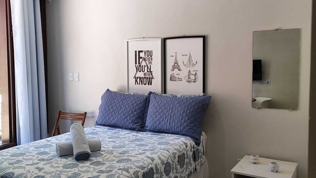 Un dormitorio con una cama, una mesita de noche, un espejo y dos cuadros en la pared.