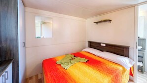 A bedroom with a bed, a wooden wardrobe, a bedside table, and a small shelf.