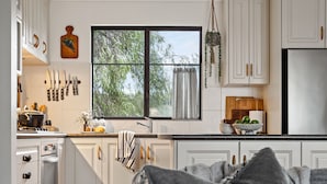 A modern kitchen with white cabinetry, a large window with a view of trees, and a hanging plant.