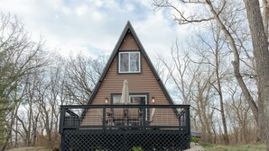 A triangular wooden cabin with a black railing and a window, surrounded by trees. - Secluded A frame cabin close Dells, BRAND NEW HOT TUB, firepit, grill. (Oxford)