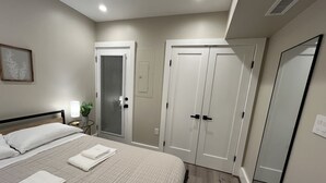 Quarto com cama, mesa de cabeceira, planta em vaso, porta e espelho.