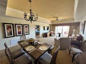 A spacious living room with a dining area, a chandelier, and a ceiling fan.