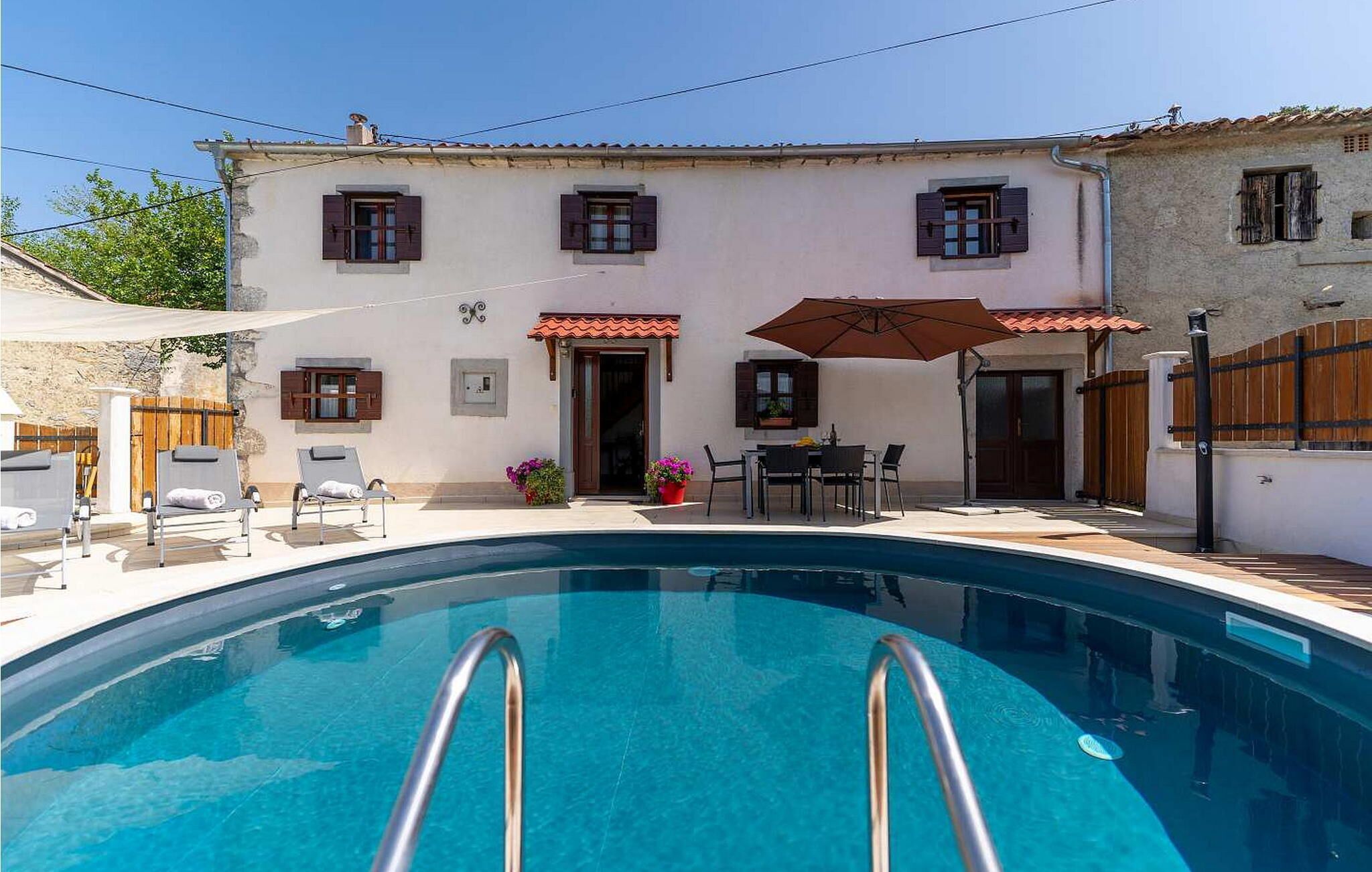 A poolside area with a pool, lounge chairs, a table with chairs, and a patio umbrella.
