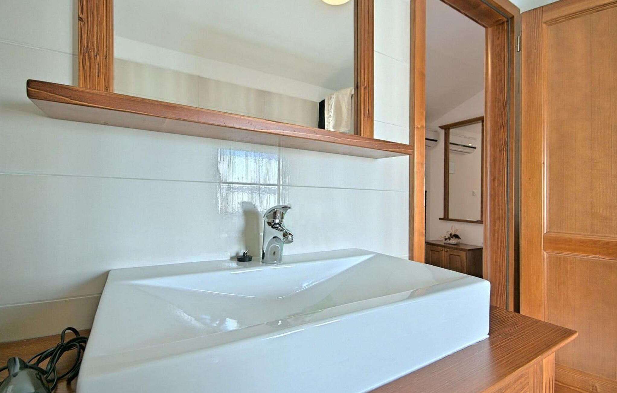 A bathroom with a white sink, wooden vanity, and a large mirror above the sink.