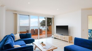 A modern living room with a large TV, blue sofas, and a balcony with a view. - Beachfront Bliss in Cowes (Cowes)