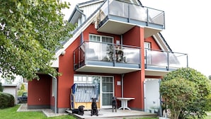A two-story building with a red exterior, a balcony on the upper floor, and a small outdoor seating area with a striped awning. - Mühlenstr. 19 Wg.2, Deutschland (Zingst)