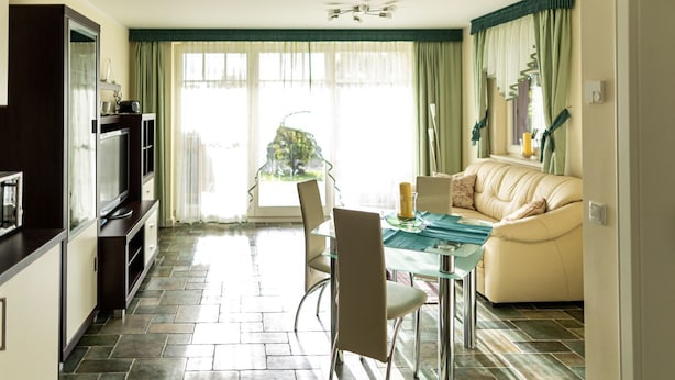A modern living room with a glass dining table, a sofa, and a kitchen area with a TV and cabinets. - Mühlenstr. 19 Wg.2, Deutschland (Zingst)