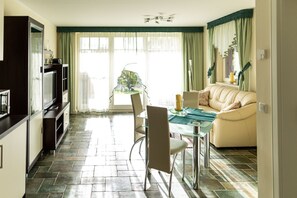 Uma sala de estar moderna com uma mesa de jantar de vidro, um sofá e uma área de cozinha com televisão e armários.