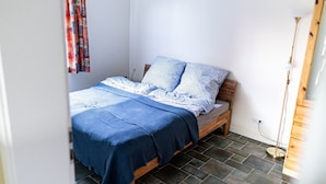 A small, neatly made bed with a blue and white patterned bedspread and pillows, a wooden headboard, and a tiled floor. - Mühlenstr. 19 Wg.2, Deutschland (Zingst)