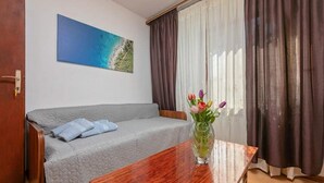 Una habitació amb un llit, una taula de fusta, un quadre d'una platja i una finestra amb cortines.