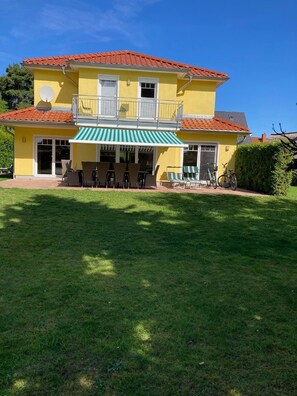 Un edificio giallo di due piani con tetto in tegole rosse, un balcone e un patio coperto con mobili da esterno.