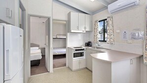 Una kitchenette compacta con microondas, horno y lavamanos, junto a una cama y un baño pequeño.