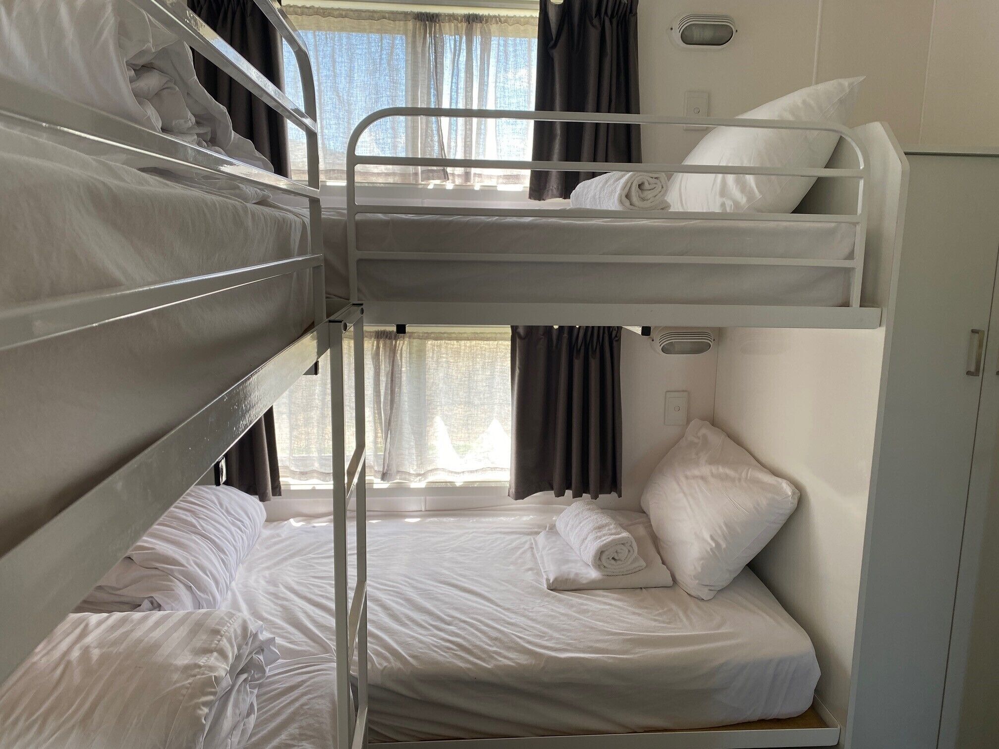 A bunk bed room with white bedding and a window with curtains.