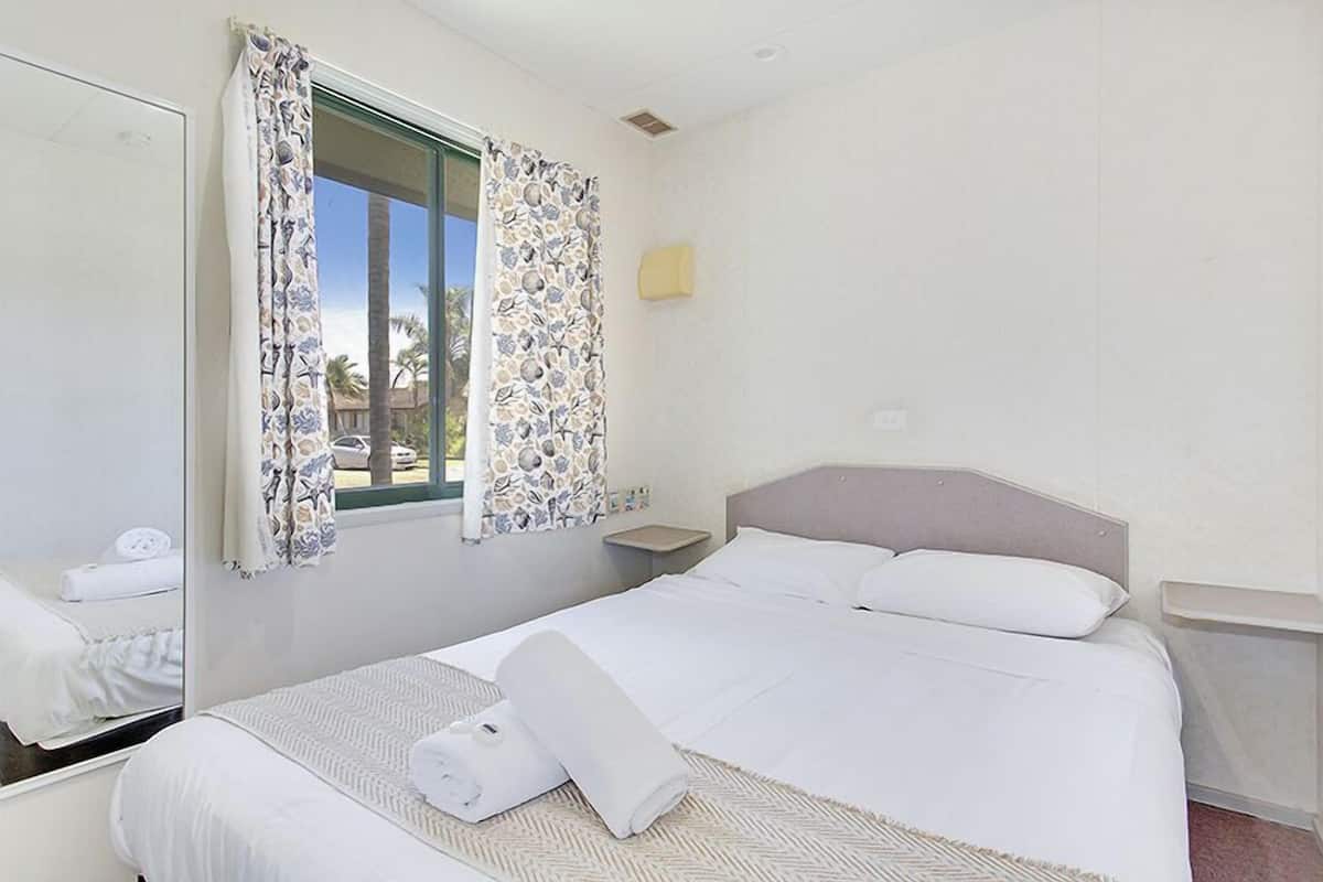 Una habitación de hotel con cama, mesita de noche, espejo y ventana con cortinas estampadas.