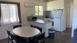 Una cocina moderna con armarios blancos, microondas, estufa y pileta. Cuenta con un comedor con mesa redonda y sillas.