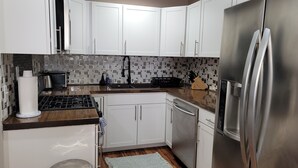 Eine moderne Küche mit weißen Schränken, einem Edelstahl-Kühlschrank, einem Gasherd und einer gefliesten Spritzschutzwand.