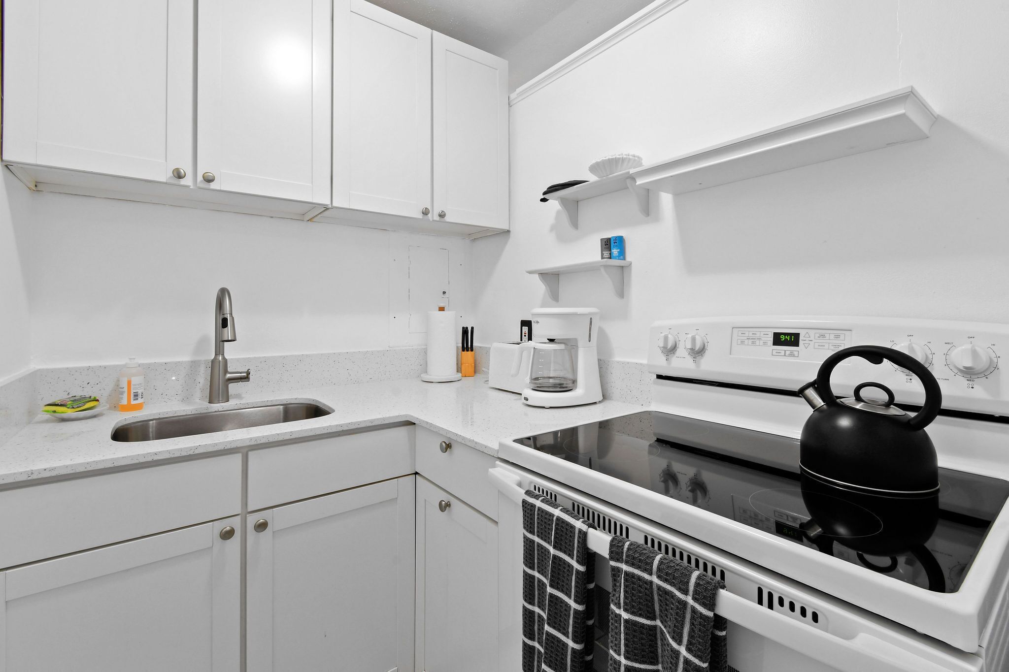 Een moderne keuken met witte kasten, een roestvrijstalen spoelbak, een waterkoker en een koffiezetapparaat.