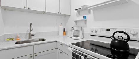 Een moderne keuken met witte kasten, een roestvrijstalen spoelbak, een waterkoker en een koffiezetapparaat.