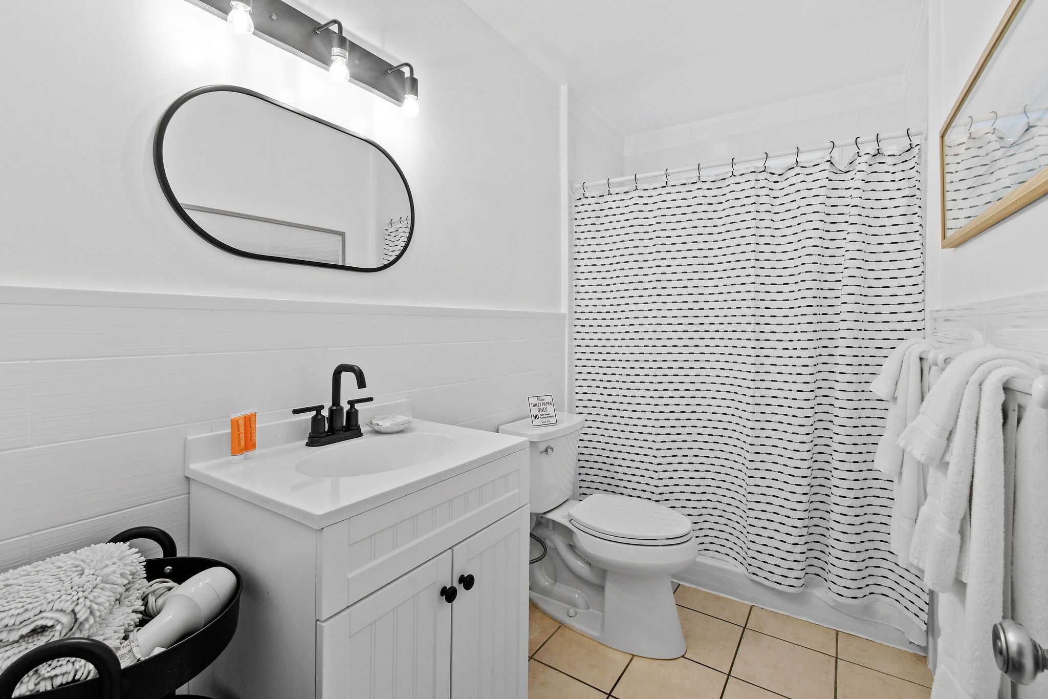 A bathroom with a white sink, mirror, and toilet. There is a black and white striped shower curtain and a white towel rack.