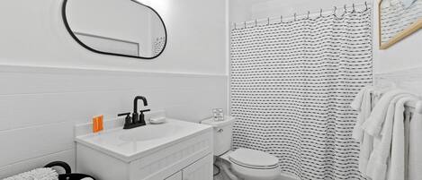A bathroom with a white sink, mirror, and toilet. There is a black and white striped shower curtain and a white towel rack.