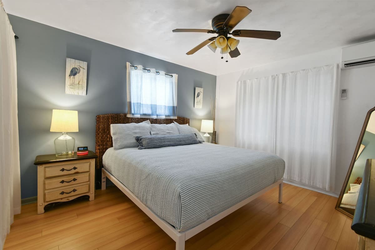 Ein Schlafzimmer mit einem Bett, Nachttischen, einem Deckenventilator und einem Fenster mit Vorhängen.