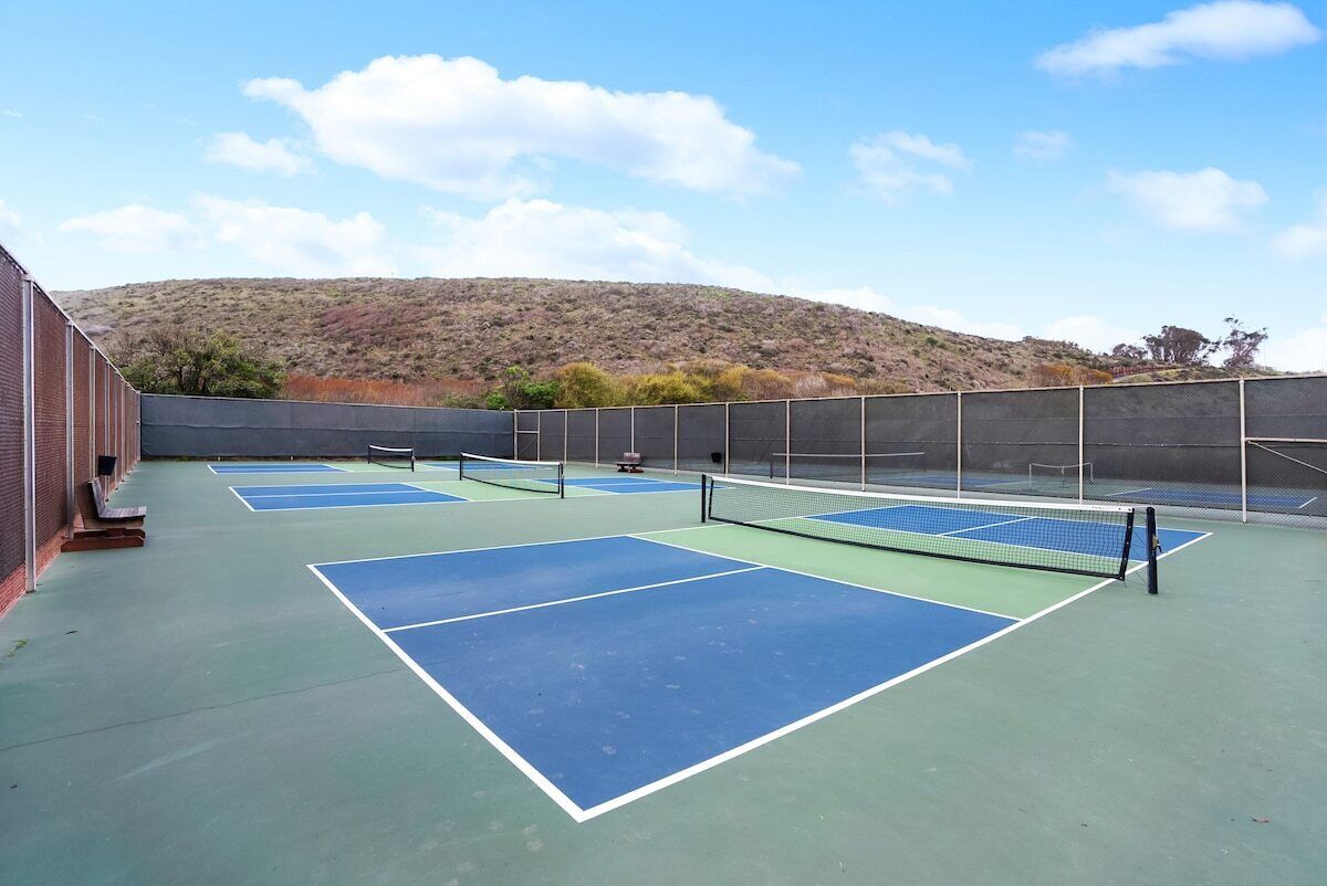 Ein Tennisplatz im Freien mit mehreren Spielfeldern, einem Netz und einer Hügelkulisse im Hintergrund.