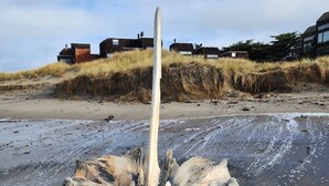 Une plage de sable avec une grande sculpture érodée par les éléments, placée au premier plan.
