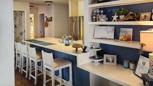 Une cuisine moderne avec des meubles blancs, un îlot central doté de tabourets et des objets décoratifs disposés sur des étagères.