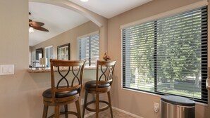 A kitchen with two wooden bar stools, a window with blinds, a trash can, and a ceiling fan. - This 1525 SqFt Upper condo Has been updated. Beautiful lake and mountain views (La Quinta)