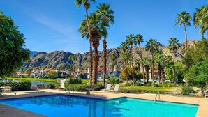 A swimming pool with clear blue water, surrounded by palm trees and a mountain backdrop. - This 1525 SqFt Upper condo Has been updated. Beautiful lake and mountain views (La Quinta)