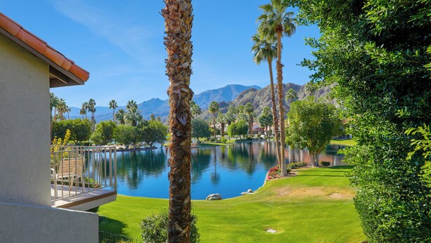 A view of a swimming pool surrounded by palm trees and a mountain backdrop. - This 1525 SqFt Upper condo Has been updated. Beautiful lake and mountain views (La Quinta)