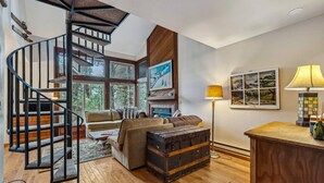 Un salón espacioso con una escalera de madera, un sofá acogedor, una chimenea y un amplio ventanal con vistas al exterior.