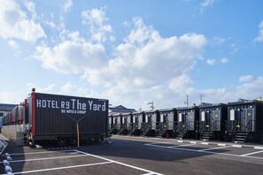 Un hotel con un contenedor grande identificado como "HOTEL R9 The Yard" estacionado en un estacionamiento.