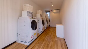 A laundry facility with multiple washing machines and dryers lined up against a wall with striped wallpaper. - HOTEL R9 The Yard Nagahama (Nagahama)