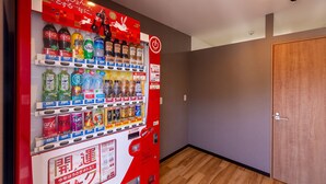 A vending machine with various drinks and snacks, a wooden door, and a hallway with wooden flooring. - HOTEL R9 The Yard Nagahama (Nagahama)