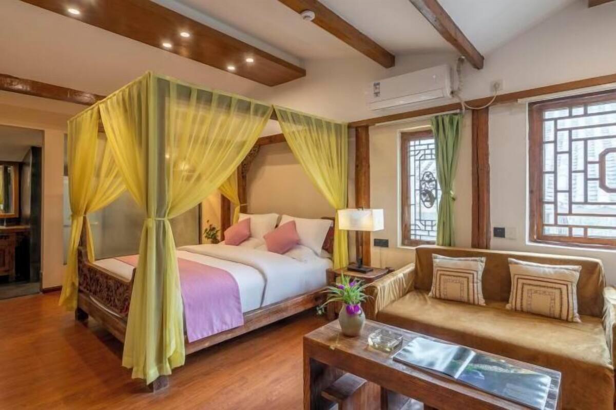Ein Schlafzimmer mit einem Himmelbett, einer Couch, einem Couchtisch und einem Fenster mit Vorhängen.