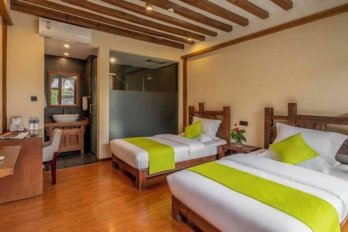 Ein Hotelzimmer mit zwei Betten, einem Holztisch, einem Waschbecken und einer Dusche.